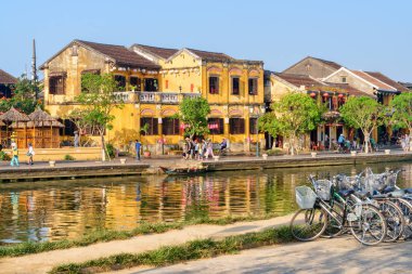 Hoi bir (Hoian), Vietnam - 11 Nisan 2018: Hoi An antik kenti tarih Prş Bon nehre yanında Bisiklet Park. Mavi gökyüzü arka plan üzerinde geleneksel sarı binalar. Set yürüyen turist.