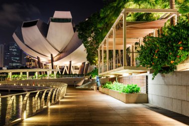 Marina Bay Singapur boyunca tahta kaldırım doğal gece manzarası. Waterfront Promenade ve alacakaranlıkta modern binalar. Şaşırtıcı cityscape.