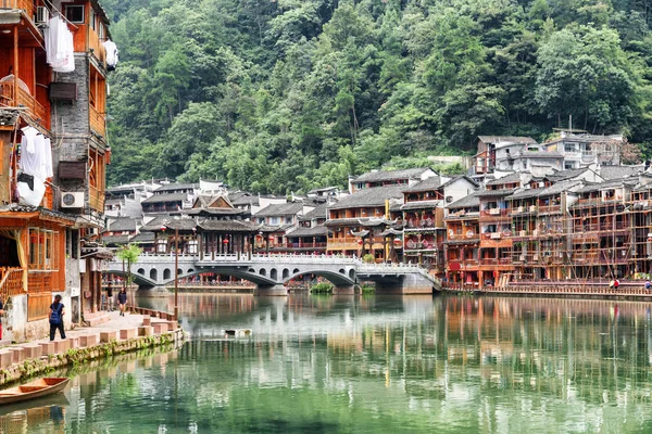Beautiful view of Phoenix Ancient Town (Fenghuang) with scenic bridge over the Tuojiang River (Tuo Jiang River) among green woods. Traditional Chinese riverside buildings reflected in water, China.