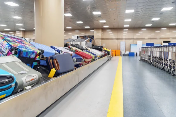 Colorful suitcases on luggage conveyor belt and row of trolleys at arrival area of passenger terminal in airport. Baggage carousel.