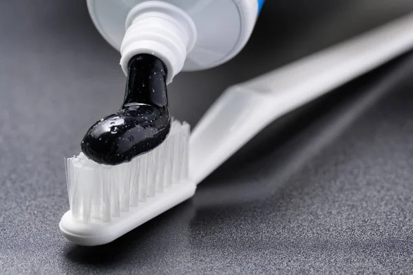 Close-up view of black charcoal whitening toothpaste being squeezed from tube on a white toothbrush. Dental health.