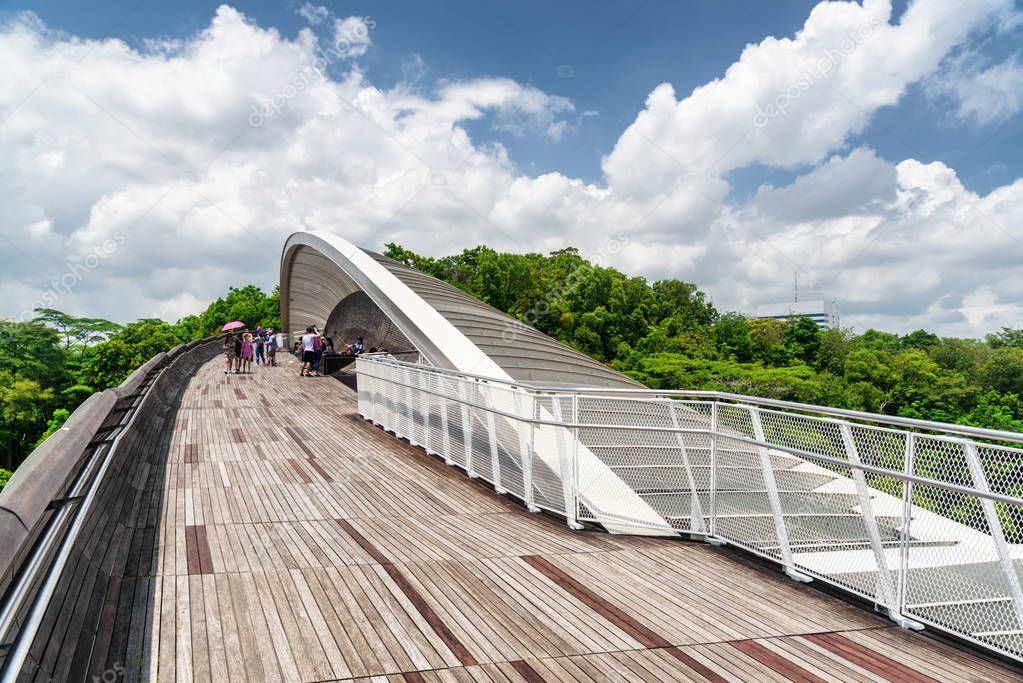 Scenic view of amazing bridge imitating a wave. Fantastical shape of the pedestrian bridge in Singapore. Curving and twisting wooden walkway leading to a green park. Beautiful cityscape.
