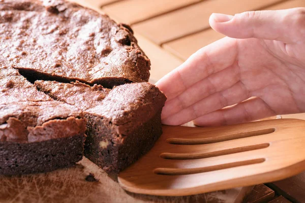 Hand taking piece of delicious chocolate cake with walnuts — Stock Photo, Image