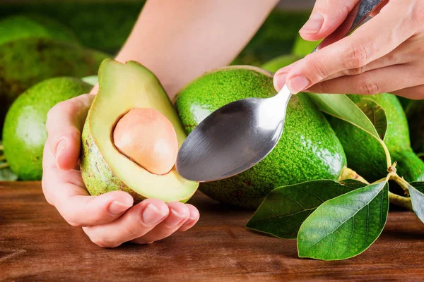 Handen van de vrouw houden lepel en de helft van avocado — Stockfoto