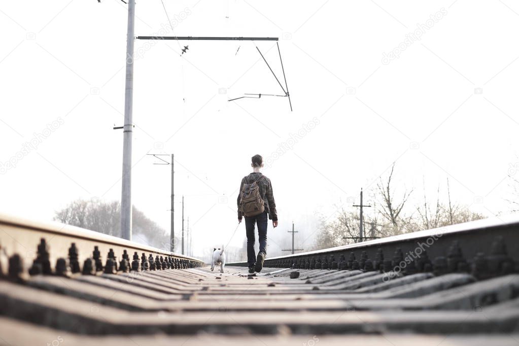 Teenager on railway walking with small white dog