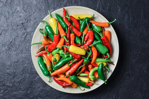 Verschillende kleuren hete pepers in houten plaat — Stockfoto