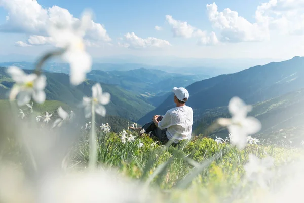 Turysta w białych ubraniach siedzi na górskiej łące — Zdjęcie stockowe