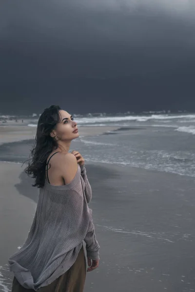 年轻女子走在狂风暴雨的海滩上 面对浓重的乌云 — 图库照片