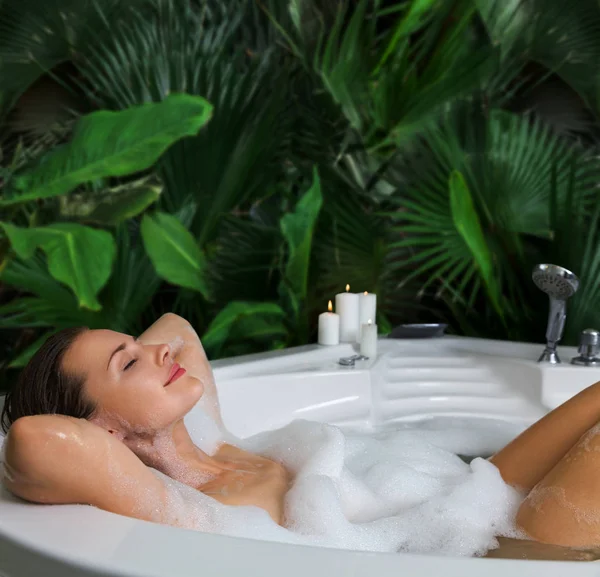 Una mujer se relaja en la bañera de hidromasaje con espuma de jabón —  Fotos de Stock