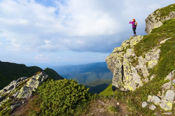 Arka torbayla sportif Kız uçurumun kenarında duran ve sonsuz üzerinde izlerken büyük güneşli gün dağlar peyzaj.