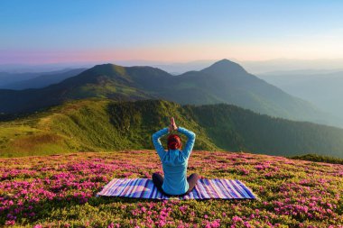 Renkli halı. Yoga-kız lotus poz. Ormangülü çiçek ile çim. Yüksek dağlar. Sihirli orman. Meditasyon. Sakin ol. Yaz sahne. Sıcak güneşin ışınları.