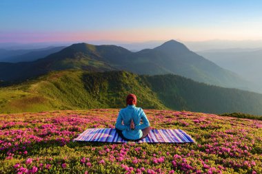 Renkli mat. Yoga-kız lotus poz. Ormangülü çiçek ile çim. Yüksek dağlar. Sihirli orman. Meditasyon. Sakin ol. Yaz sahne. Sıcak güneşin ışınları.