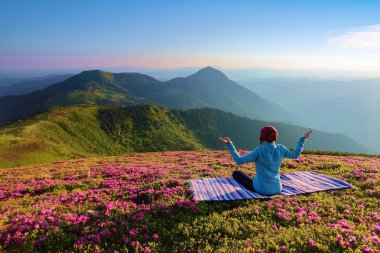 Ormangülü çiçek arasında'nın bahçesinde yoga-kız poz renkli halının üstünde oturuyor. Meditasyon. Sis dağlarda, yatay. Güzel yaz sahne.