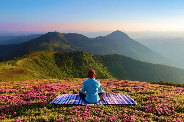 Ormangülü çiçek arasında'nın bahçesinde yoga-kız poz renkli halının üstünde oturuyor. Meditasyon. Sis dağlarda, yatay. Güzel yaz sahne.