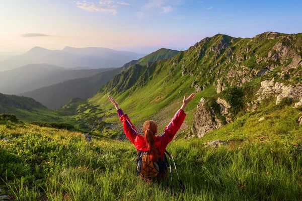 The tourist girl with back sack and tracking sticks sits on the lawn. Relaxation. Mountain landscapes. Wonderful summer day. Scenery.