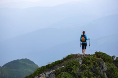 İzleme sopa ve arka torba uçurumun kenarında turist kızla. Manzara yüksek dağlarla. Sonsuz çokluk ufukta. Sıcak güneşli yaz gün.