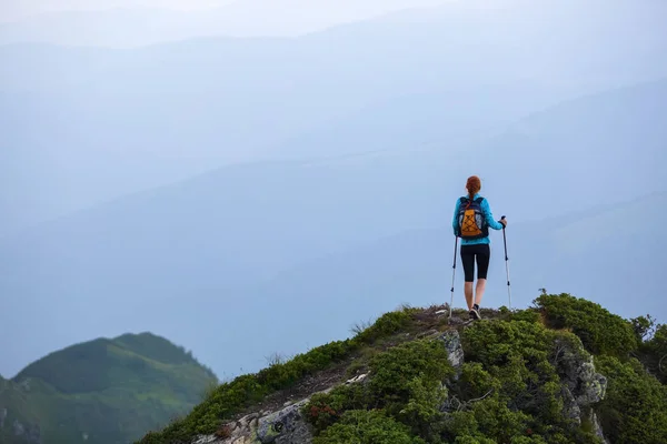 在悬崖边上有追踪棍和后袋的旅游女孩 风景与高山 无尽无垠的地平线上 温暖阳光明媚的夏日 — 图库照片