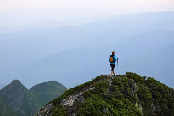 那个带着旅游设备的女孩爬上了岩石高高的山顶和草坪 雾中群山之景 — 图库照片