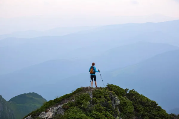 那个带着旅游设备的女孩爬上了岩石高高的山顶和草坪 雾中群山之景 — 图库照片