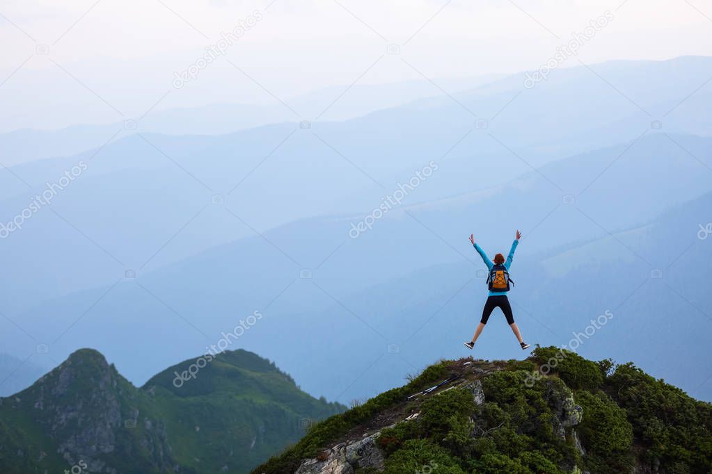 Funny frozen poses while jumping. The girl in tennis shoes. The lawn at the edge of the cliff with rocks. Vastness with mountains. Fantastic summer scenery.