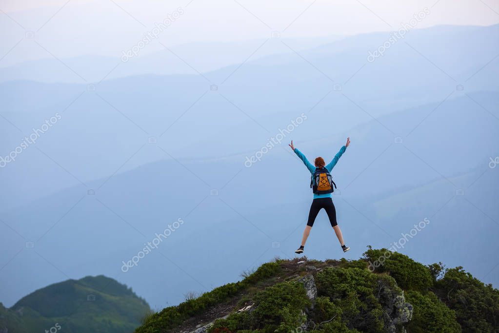 Funny frozen poses while jumping. The girl in tennis shoes. The lawn at the edge of the cliff with rocks. Vastness with mountains. Fantastic summer scenery.