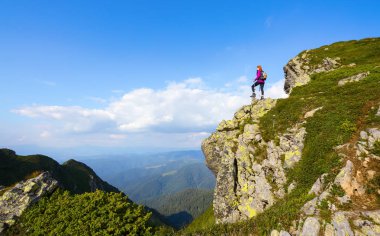 Arka torbayla sportif kız uçurumun kenarında duran ve sonsuz üzerinde izlerken büyük dağlar peyzaj güneşli gün. Güzel bahar manzara.