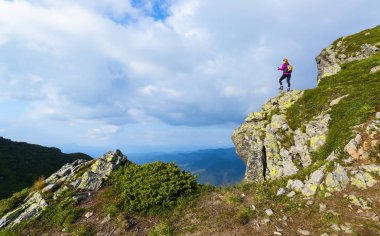 Arka torbayla sportif Kız uçurumun kenarında duran ve sonsuz üzerinde izlerken büyük güneşli gün dağlar peyzaj.