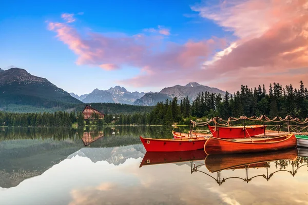 Beautiful high mountains around the incredibly magic lake with red boats and canoe on a spring day.