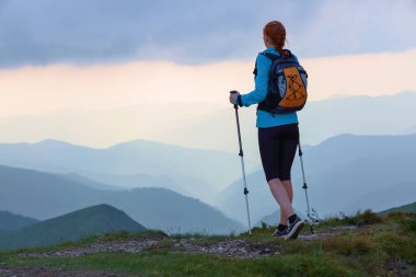 Arka çuval ve sopa izleme turist kızla çimenlerin üstünde kalıyor. Güzel bulutlu gökyüzü. Dağlardaki güneş ışınları düşmek. Yaz sahne. . Eko turizm laisure zaman.