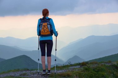 Arka çuval ve sopa izleme turist kızla çimenlerin üstünde kalıyor. Güzel bulutlu gökyüzü. Dağlardaki güneş ışınları düşmek. Yaz sahne. Eko turizm laisure zaman.