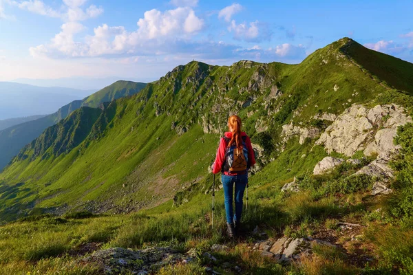 O görünümle yüksek rocky Dağları. Genç bir kız çiçekleri arasında yeşil çimenlerin üzerinde duruyor. Sur ışınları. Güzel bulutlar gökyüzünde yavaş yavaş hareket ediyor.