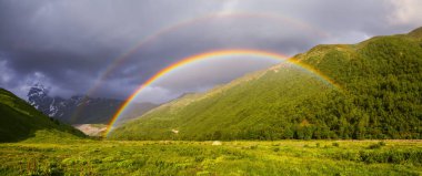 Bir turist çadır yüksek yeşil dağların arasında çim üzerinde duruyor ve bir parlak renkli rainbo bir yaz gününde göründü. Üst Svaneti, Georgia, Avrupa. Mutlu bir yaşam tarzı. Güzel evren.