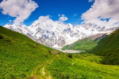 Taşlar ile geniş yoldan görüldü son derece güzel yeşil tepeler ve kayalık olan dağ karla kaplı olabilir. Üst Svaneti, Georgia, Avrupa. Mutlu bir yaşam tarzı. Güzel evren.  