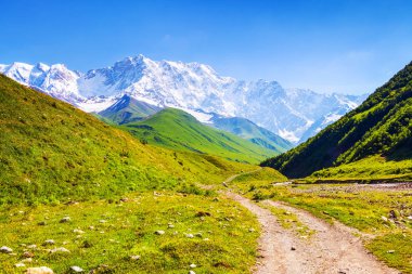 Taşlar ile geniş yoldan görüldü son derece güzel yeşil tepeler ve kayalık olan dağ karla kaplı olabilir. Üst Svaneti, Georgia, Avrupa. Mutlu yaşam tarzı.