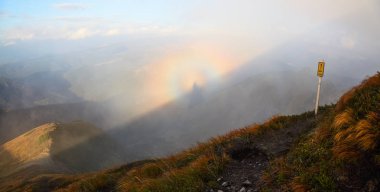 Çim turuncu çim ile gelen yüksek dağlar, mavi gökyüzü panoraması ile bulutlar ve sis Brocken Spectre bir sonbahar gününde açılır.