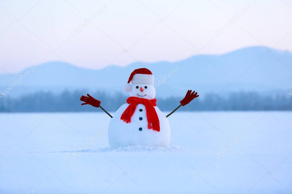 Snowman in red hat and scarf. Christmas scenery. High mountains at the background. Ground covered by snow. Nice cold winter day.