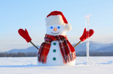 Kardan Adam ekose eşarp, kırmızı şapka, eldiven ve Icicle'ı elinde. Güzel manzara ile arka planda dağlar. Alan karla kaplı. Soğuk kış günü.