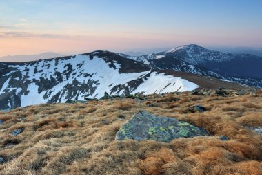 Panoramik Dağları kar ile kaplı sabaha ışıklı alır, belgili tanımlık çim açık gelen güneş ışınları. Güneş doğuyor. Büyüleyici bahar manzara.