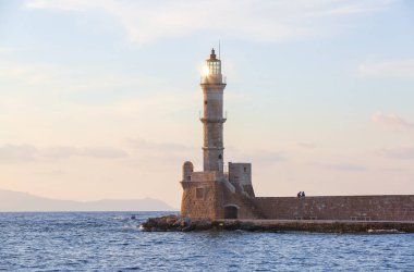Tuğladan yapılmış yüksek, güzel, antik deniz feneri. Muhteşem gün batımı gökyüzünü aydınlatAn. Deniz kıyısı boyunca bir duvar ve yol vardır. Turistik tatil Chania, Creete adası, Yunanistan.