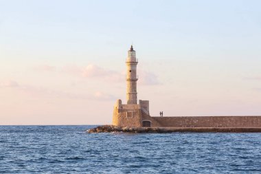 Tuğladan yapılmış yüksek, güzel, antik deniz feneri. Turistik tatil Chania, Creete adası, Yunanistan. Muhteşem gün batımı gökyüzünü aydınlatAn. Deniz kıyısı boyunca bir duvar ve yol var..