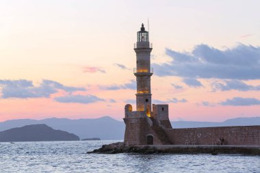 Lambalar akşam saatlerinde deniz fenerini aydınlatıyor. Antik mimari. Liman Chania konumu, Creete adası, Yunanistan. Günbatımı. Dağlar ve deniz ile manzara.