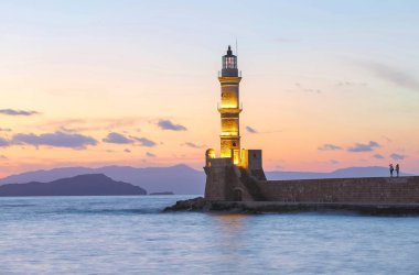Lambalar akşam saatlerinde deniz fenerini aydınlatıyor. Antik mimari. Liman Chania konumu, Creete adası, Yunanistan. Günbatımı. Dağlar ve deniz ile manzara.