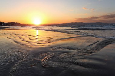 Yer yer Agia Marina Beach, ada Girit, Yunanistan. Deniz kıyıları kayaların arasında sarkıyor, gün doğumu ıslak kuma yansıyor. Ufukta sis içinde dağlar. Yüksek dalgalar ile Fırtına deniz.