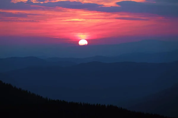 Fantástica puesta de sol ilumina el cielo con colores maravillosos: rosa brillante, amarillo, naranja. El paisaje de las montañas silueta en el crepúsculo. Nubes inusuales. Ubicación las montañas de los Cárpatos . — Foto de Stock