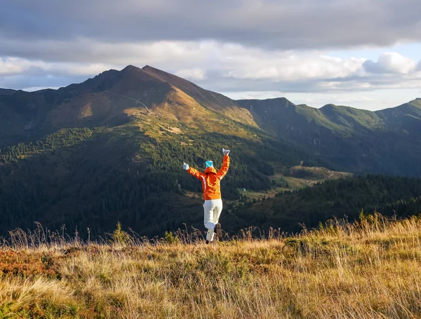 快乐的女运动员在草坪上跳着。 秋天的风景,高山,森林,晴天的天空,云彩. — 图库照片