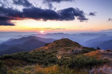 İnanılmaz bir gün batımı. Sonbahar güneşli bir gün. Dağların manzarası. Mutlu turist tepede kalır. Güneş ışınları gökyüzünü ve ufku aydınlatıyor. Turistik bölge Karpatyalı, Ukrayna Avrupa.