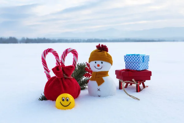 Christmas composition. Snowman with red sack, colorful gift box on the sledge, striped heart shaped candies and smile icons emoji. Happy new year 2020. — Stock Photo, Image