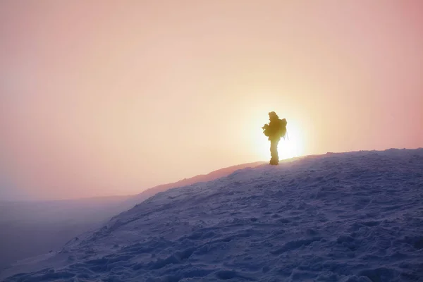 बर्फाने झाकलेल्या लॉनवर कोणीतरी उभे आहे. विलक्षण सूर्योदय. पर्वत सह लँडस्केप गुलाबी रंग किंवा छटांमध्ये सकाळी धुके . — स्टॉक फोटो, इमेज