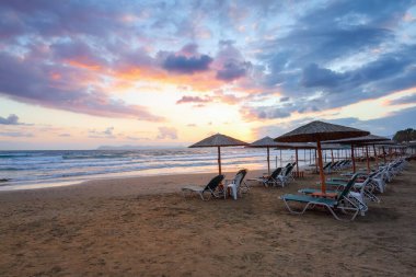 Şemsiyeli ve şezlonglu boş bir sahil. İnanılmaz bir gün doğumu. 2020 yaz karantina seyahati. Güzel yaz manzaralı deniz manzarası. Yunanistan Girit adasında rahatla.