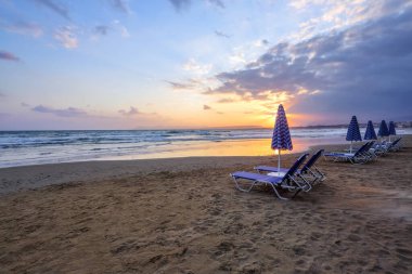 Gün doğumu. Karantinadan sonra turistleri bekleyen renkli şemsiyeleri ve şezlongları olan çöl sahilleri. Güzel yaz manzaralı deniz manzarası. Yunanistan Girit Adası 'nda rahatla. Metin için boş alan.